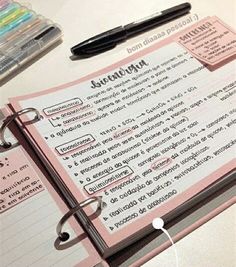 a pink notebook with some writing on it and a pen next to it, sitting on a table