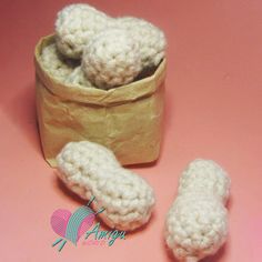 two crocheted shoes are next to a small basket of white balls on a pink surface