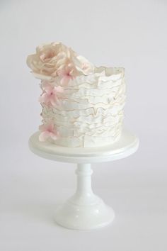 a white cake with pink flowers on top sitting on a pedestal in front of a white background