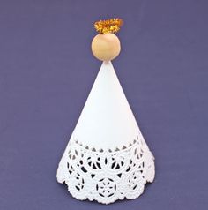 a small white cake cone with a wooden top on a purple surface, decorated with lace and beads