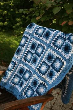 a blue and white crocheted blanket sitting on top of a wooden chair next to a tree