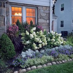 a garden with flowers and bushes in front of a house