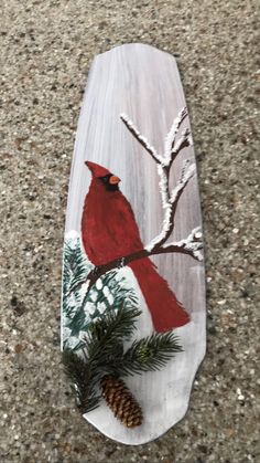 a skateboard with a cardinal painted on it and pineconis in the background