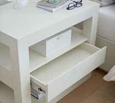 a white table with some books and glasses on it next to a bed in the background