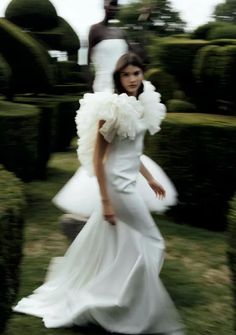 a woman in a white dress walking through some hedges