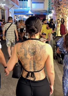 the back of a woman's body with tattoos on it and people walking around