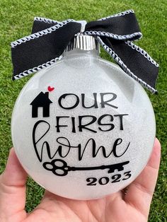 a hand holding a glass ornament with the words our first home on it