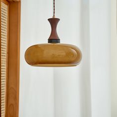 a wooden light hanging from a ceiling in front of a white curtain and window with curtains behind it