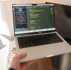 a person holding up a laptop computer in their left hand, with the screen turned on