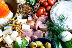 an assortment of meats, cheese and vegetables on a wooden table with dipping sauce