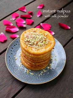 a stack of pancakes sitting on top of a blue plate next to pink flower petals