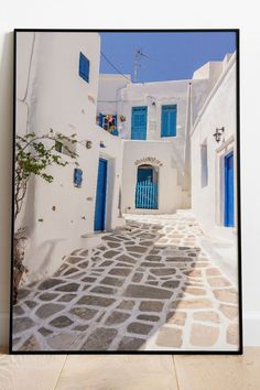 a framed photograph of an alleyway with blue doors and shutters in oia, greece