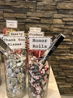 two glass jars filled with coins on top of a white counter next to a stone wall