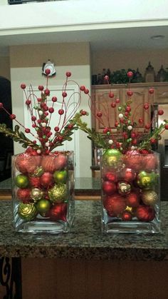 two clear vases filled with ornaments on top of a kitchen counter covered in greenery