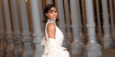 a woman in a white dress posing for the camera with columns behind her and one hand on her hip