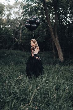 a woman in a black dress is walking through the grass with balloons on her head