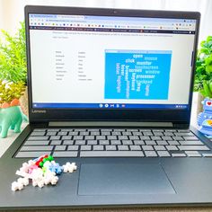 an open laptop computer sitting on top of a desk next to toy animals and plants