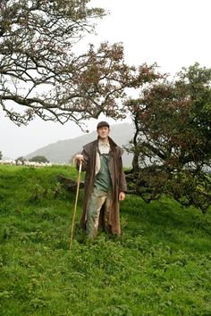 a man standing on top of a lush green field next to a tree filled with leaves