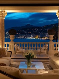 a living room filled with furniture and a view of the ocean at night in front of a balcony