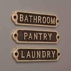 three bathroom name tags are shown on a gray surface, one is gold and the other is black