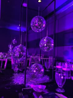 disco balls hanging from the ceiling at a party with purple lighting and silverware on the table