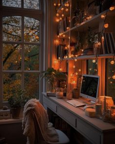 a desk with a computer on top of it next to a window filled with lights