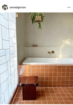 a bath tub sitting next to a wooden bench in a room with tiled walls and floor