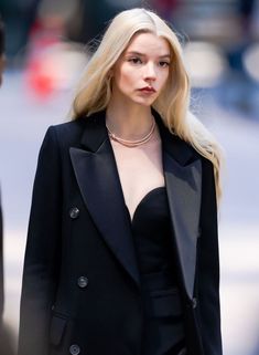 a woman with blonde hair wearing a black suit and choker necklace on the street