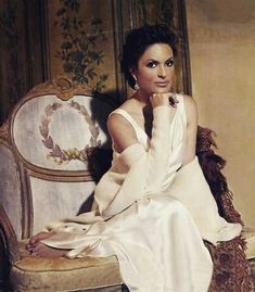 a woman sitting on top of a chair wearing a white dress and holding her hand under her chin