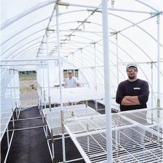 two men are standing in a greenhouse with white plastic structures and metal grates on the floor