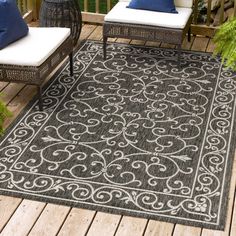 an outdoor rug on a deck with chairs and plants in the foreground, along with blue pillows