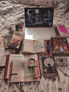 an open laptop computer sitting on top of a bed covered in books and other items