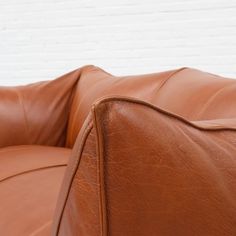 a brown leather couch sitting in front of a white brick wall