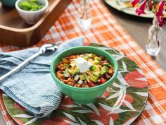 a green bowl filled with food sitting on top of a colorful place mat next to a wooden tray