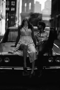 a man and woman sitting on the hood of a car