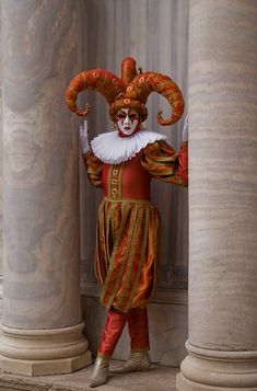 a man dressed as a clown standing next to two pillars with columns in the background