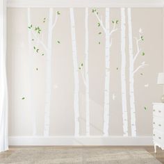 a white wall with trees painted on it and a lamp next to the dresser in front