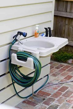 a white sink sitting on the side of a house next to a garden hose holder