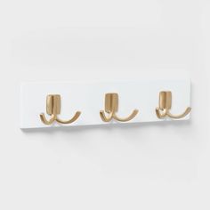 three gold hooks on a white coat rack with two coats hanging from the top and bottom