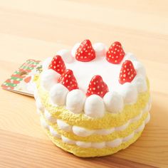 a yellow cake with white frosting and strawberries on top, sitting on a wooden table