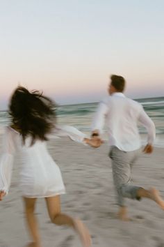 two people running on the beach holding hands