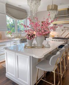 a white kitchen with gold accents and pink flowers in vases on the center island