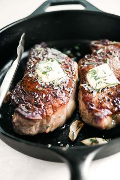 two steaks are cooking in a skillet with butter and herbs on the side