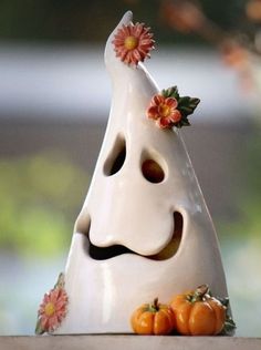 a white vase with flowers on it sitting on top of a table next to pumpkins