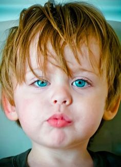 a close up of a child with blue eyes wearing a black shirt and looking at the camera