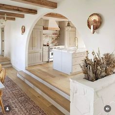 a kitchen with white walls and wooden flooring next to a dining room table in front of an archway