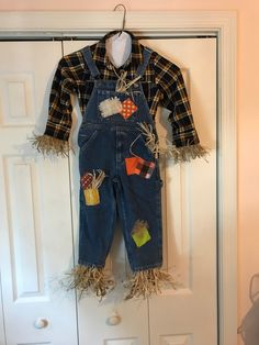 a child's jean overalls with patches and fringe on the legs hanging from a door