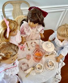 a group of dolls sitting around a table with plates and cups on top of it