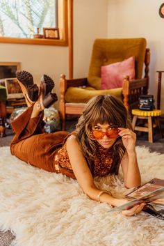 a woman laying on the floor reading a book and looking at her camera while wearing sunglasses