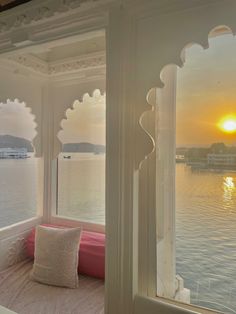 the sun is setting over the water from inside a room with white walls and windows